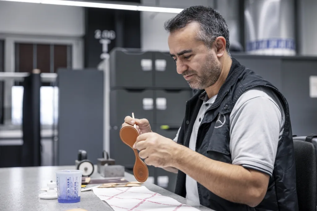 메르세데스-벤츠 마누팍투어 스튜디오 Handwerkskunst auf höchstem Niveau: Geschickte Hände sind in der MANUFAKTUR Sindelfingen die wertvollsten Werkzeuge: Spezialisten mit umfangreicher Erfahrung Beledern, Schneiden, Besticken oder Nähen in akribischer Präzision. Craftsmanship at the highest level: Skilled hands are the most valuable tools in the MANUFAKTUR Sindelfingen. Specialists with extensive experience meticulously upholster, cut, embroider, or sew with meticulous precision.